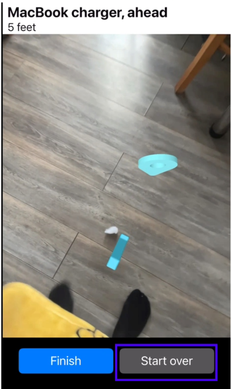 A Find My Things screen reading 'MacBook charger, ahead — 5 feet', showing the live camera view of a wooden floor with the charger highlighted, and a 'Finish' and 'Start over' button pair at the bottom. 'Start over' is picked out, because it is how a user clears a false lead and re-runs the search.